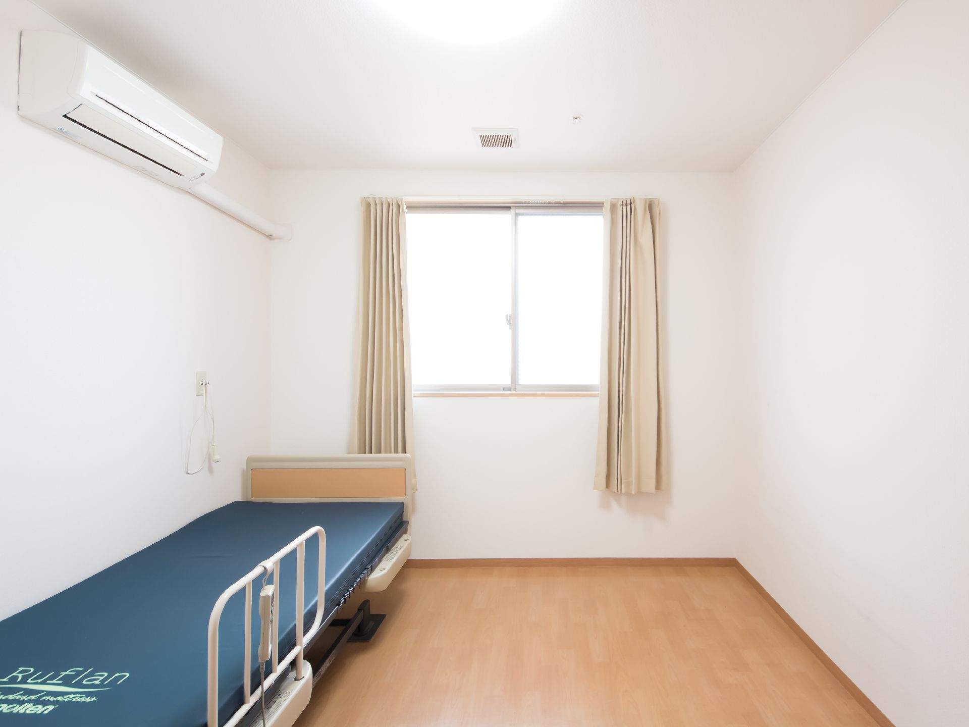 ベージュのカーテンが掛けられた腰高窓がある、白い壁紙を張った部屋