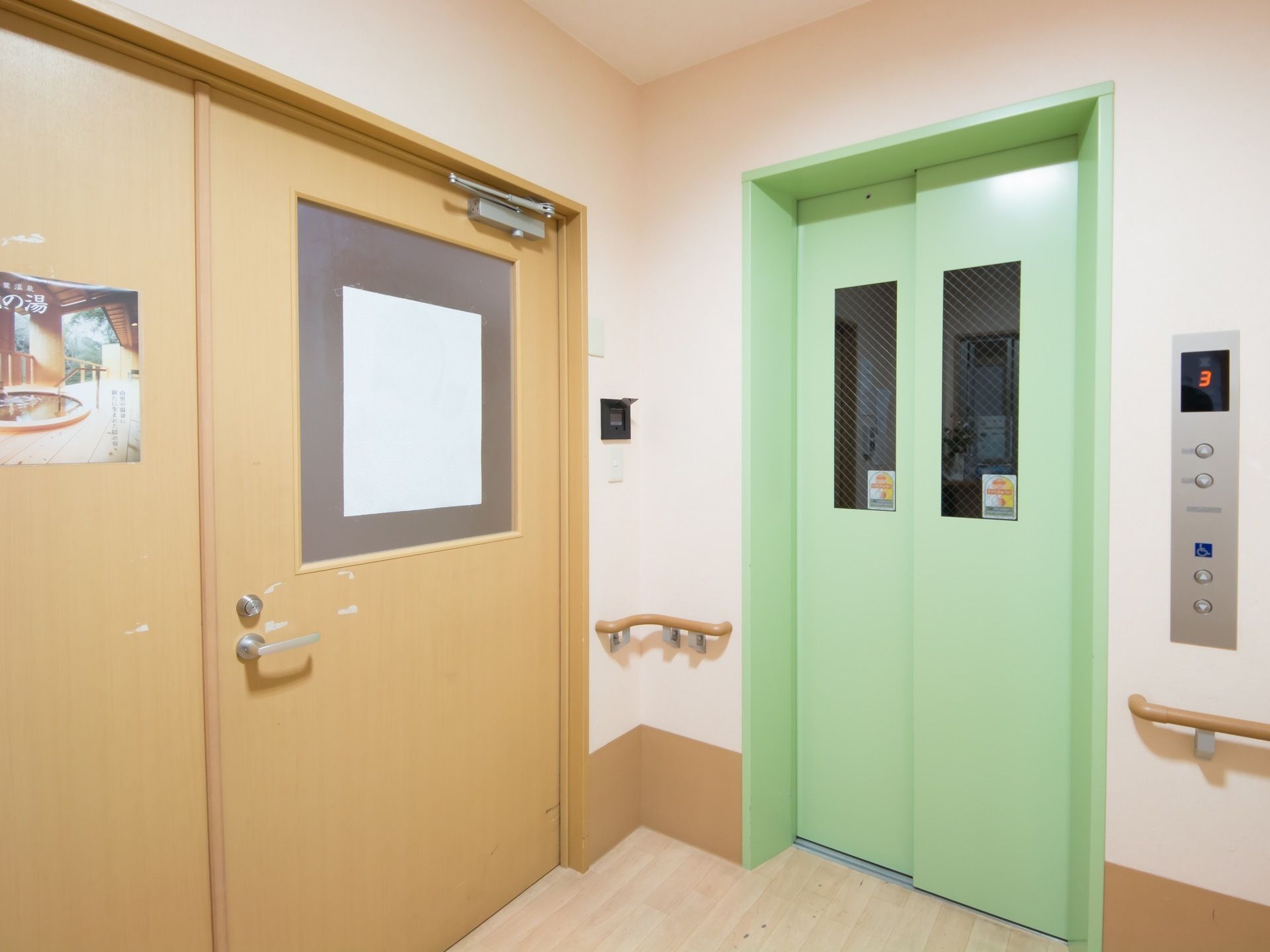 緑色の乗降口のエレベーターが設置されている。扉にはガラスがはめ込まれていて、中の様子が見えるようになっている。