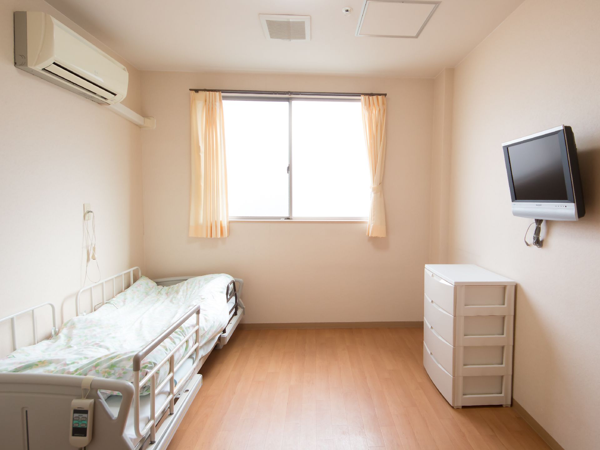 壁掛けのテレビや介護ベッドなどの設備が置かれた部屋