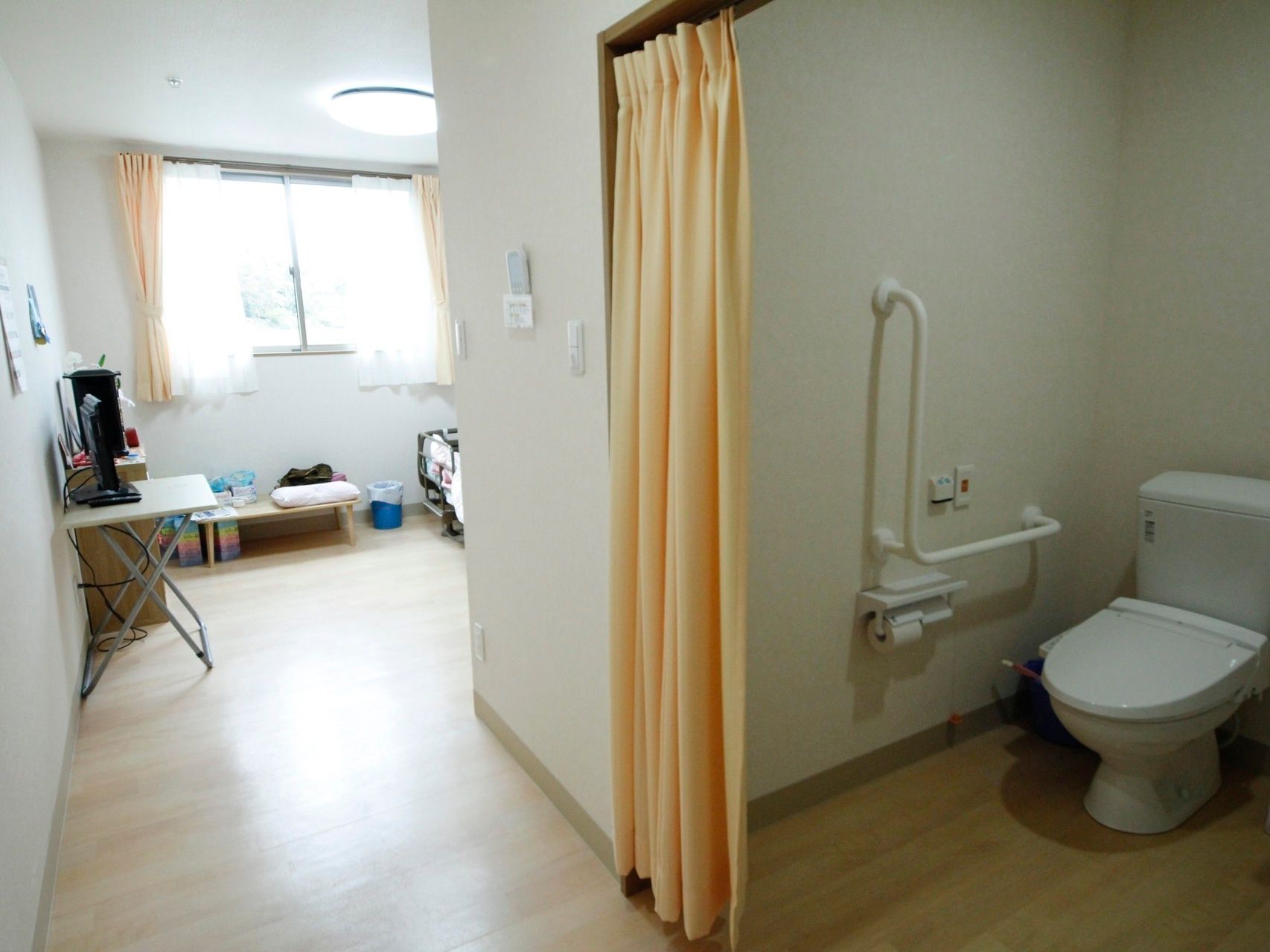 部屋の中にトイレがあり、ベージュのカーテンで仕切ってあるので、入りやすくなっている。手すりがあり、使いやすい。