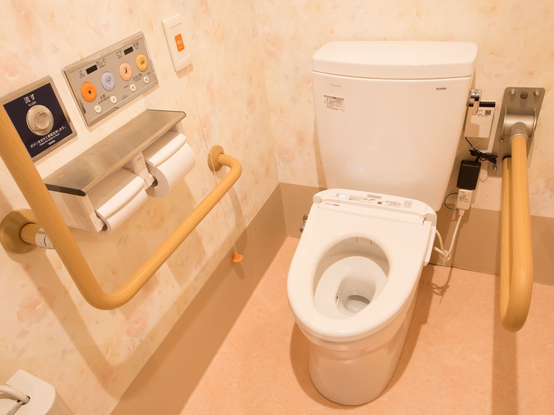 温水洗浄便座器を完備したトイレである。壁には呼び出しブザーや手すりが設置され、安全面も配慮されている。