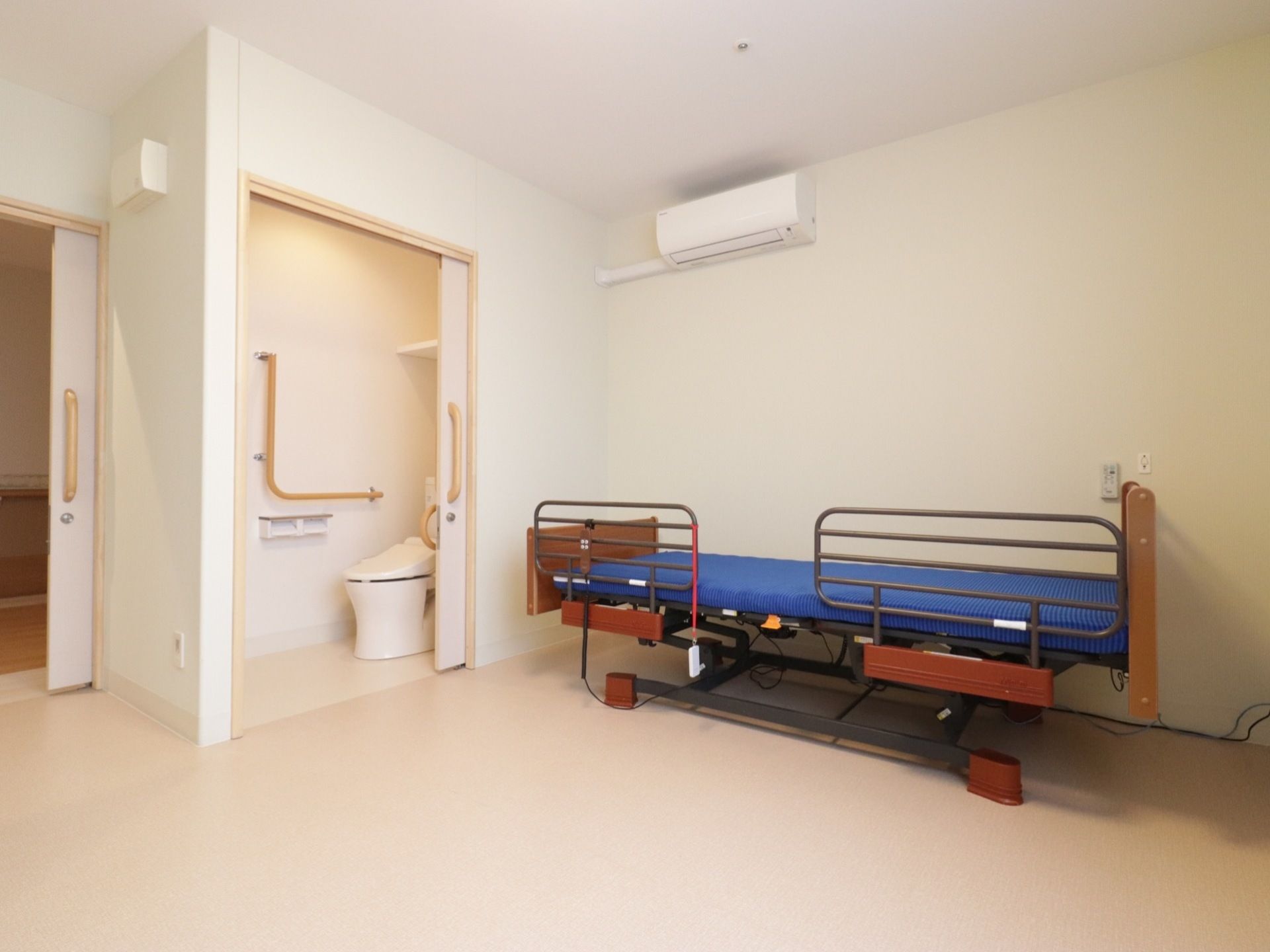白い壁紙が貼られていて、清潔な印象の居室だ。出入り口やトイレの扉は全て引き戸になっている。エアコンも完備されている。