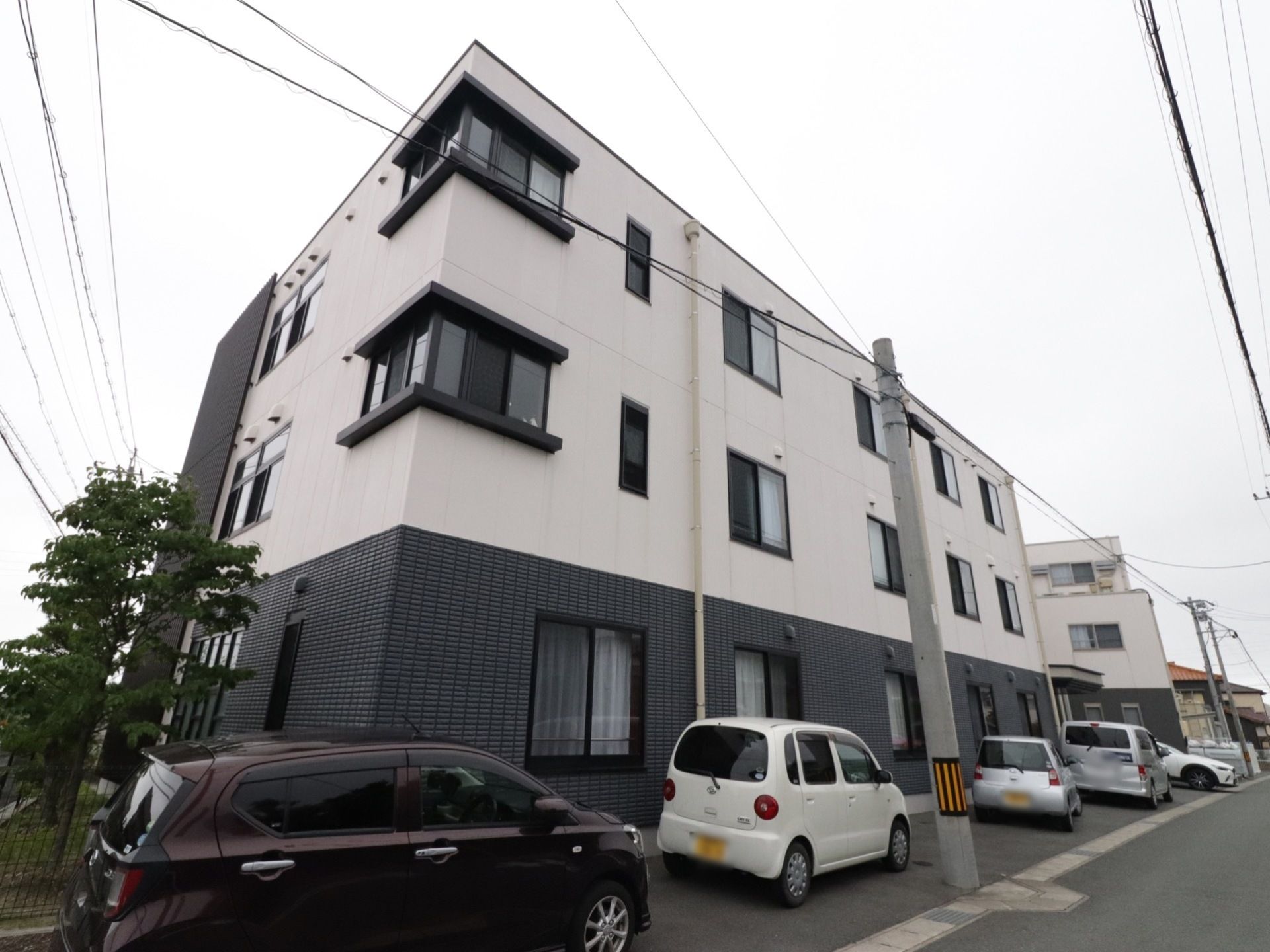 １階はグレーのタイル調、それ以外は白色の壁でデザインされた３階建ての建物