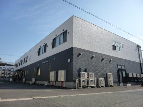 白と黒のツートーンカラーがオシャレな外観である。室外機や換気口が並んでおり、2階には多くの窓がついている。