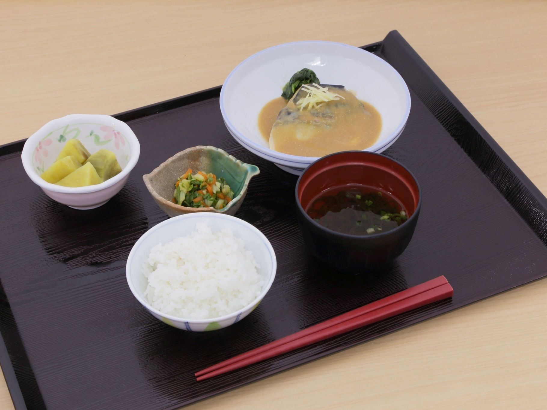 食事の一例である。ご飯、みそ汁、サバの味噌煮、野菜のお浸しが並んでいる。デザートとして、グリーンキウイが添えてある。