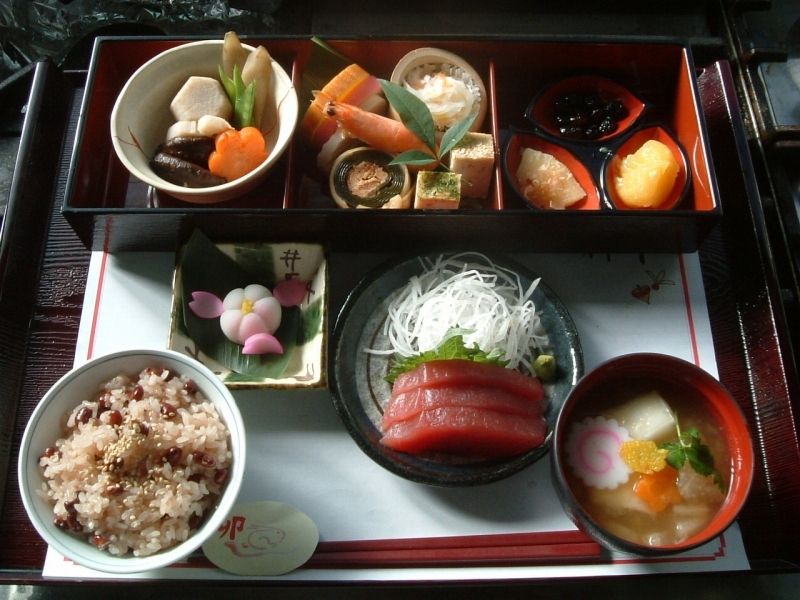 海老や栗きんとんや黒豆の入ったおせち料理と赤飯と刺身と吸い物のセット