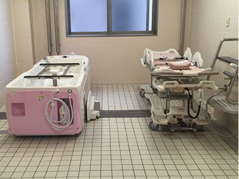 排水溝を設けてタイルを敷いた部屋に置かれた機械浴槽と介助用のストレッチャー