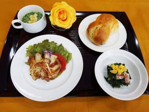 メインが鶏肉料理のパン食の献立が黒いプレートに並べられている。栄養バランスが考慮され、色彩豊かに盛り付けられている。