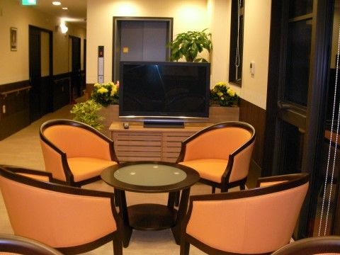 座面や背もたれ部がオレンジ色の椅子4脚と、やや低めの円形のテーブルのセットがある。奥には木製の台にのったテレビがある。