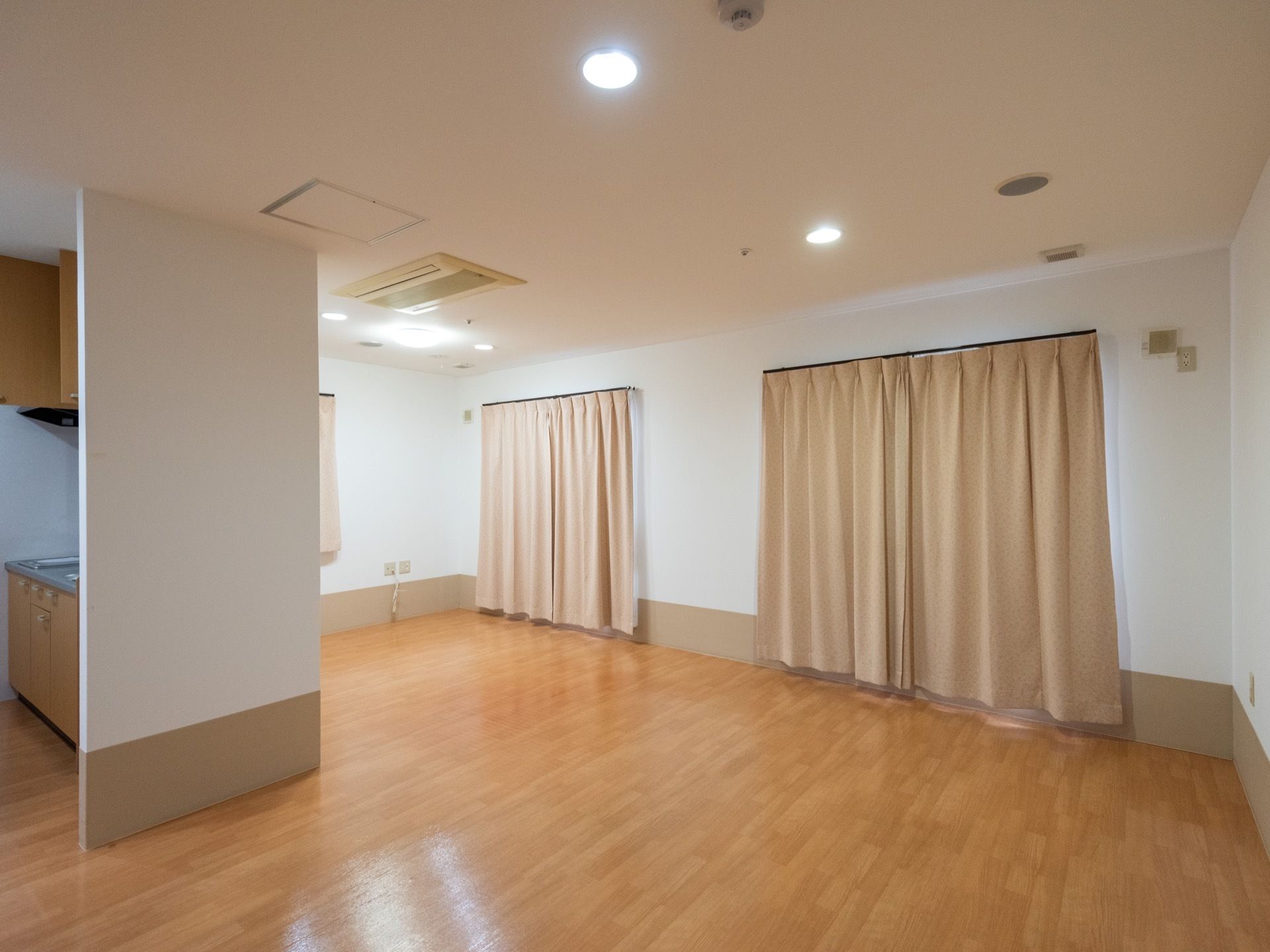 白い壁に木目調のフローリングで設計されているご入居前の居室である。ビルトインのエアコンやキッチンが完備されている。