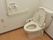 ウオッシュレット式のトイレの右手側に手すりとトイレットペーパーが付いており、その向こうに呼び出しベルがある。