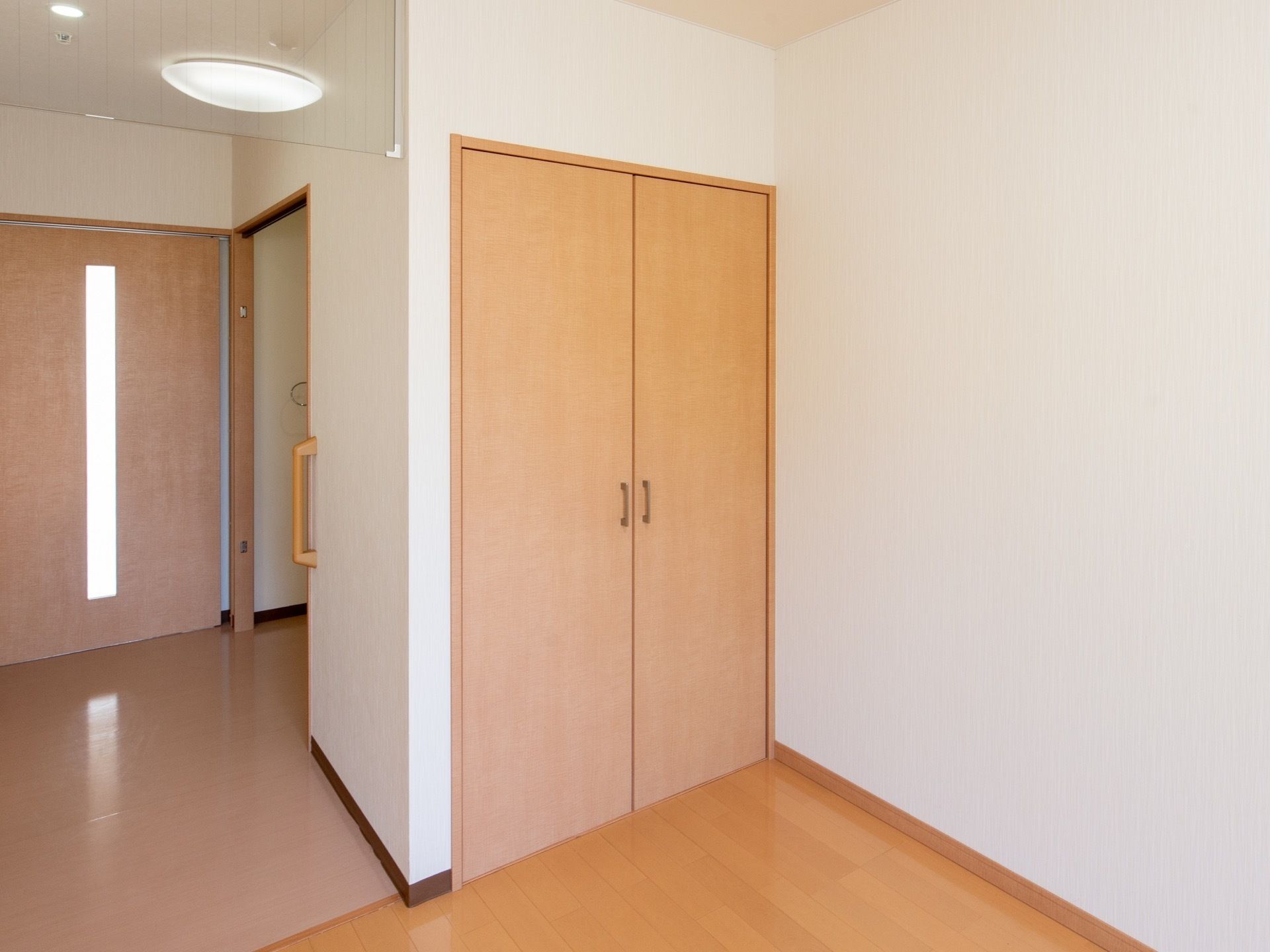 居室内に完備されている収納クローゼットである。明るい木目調の両開きの扉には、中央に取っ手が設置されている。
