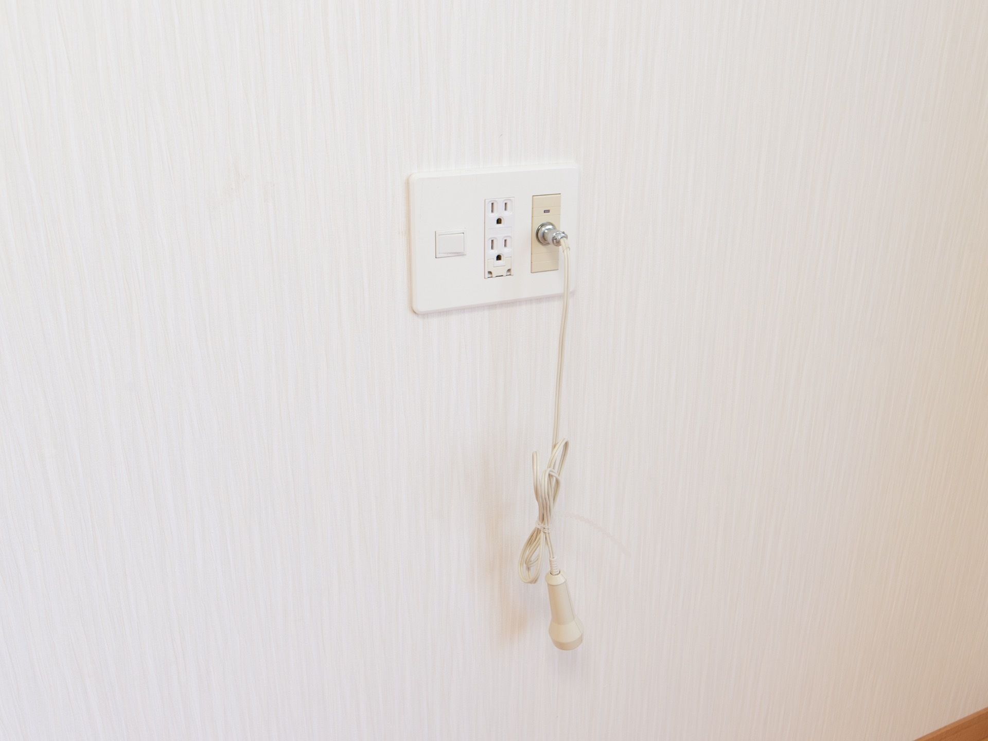 白い壁に緊急呼び出しブザーが設置されている。プラグの横には、コンセントが2口ついている。急な体調変化の際も安心である。