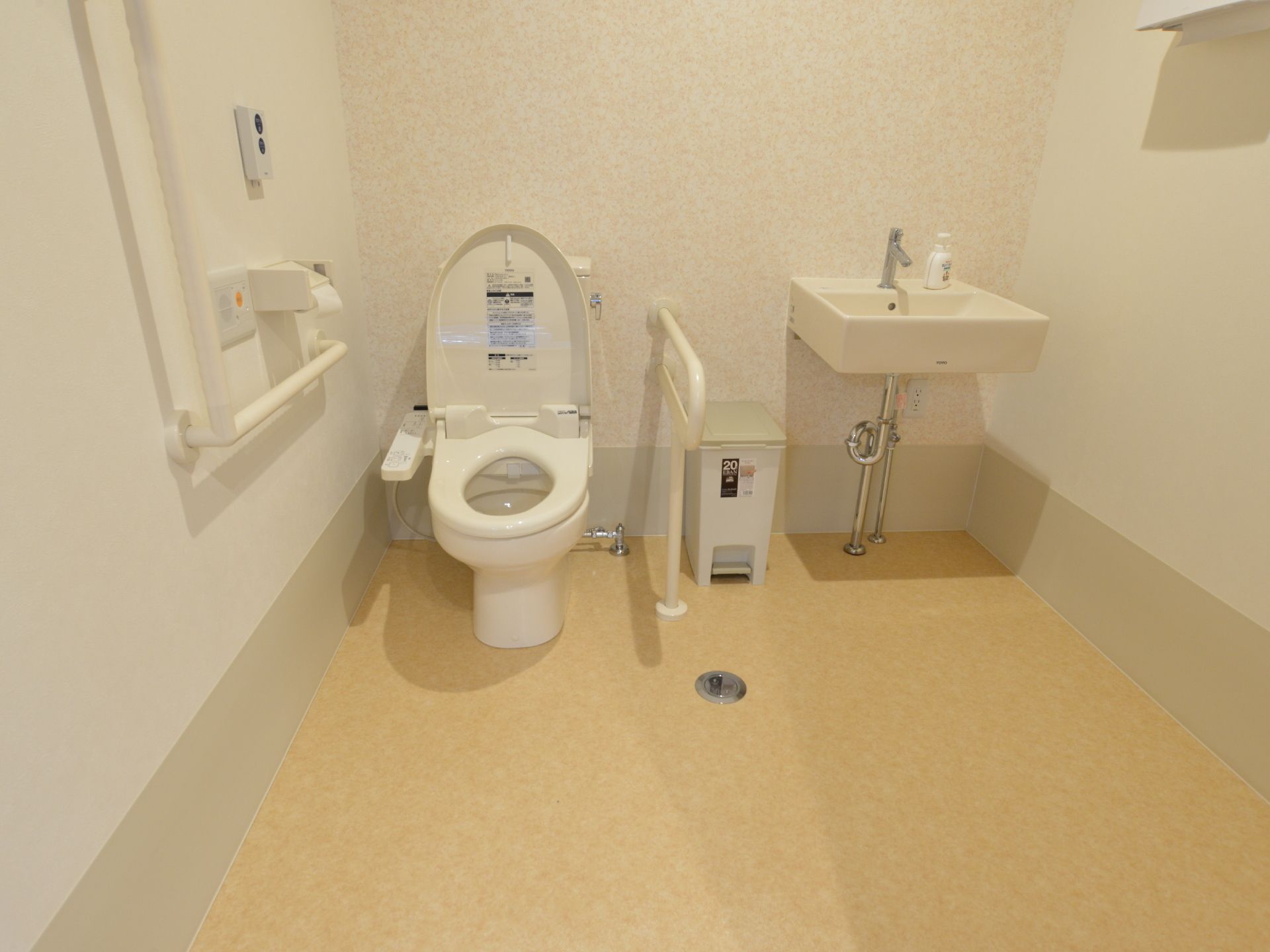 広々としたスペースに温水洗浄便座付きトイレと洗面台がある。トイレ両側には手すりがあり、洗面台横には手拭き用の紙タオルが設置されている。