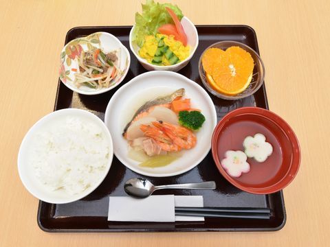 黒いお盆の上に魚料理を中心とした和食が並んでいる。メイン料理と副菜、汁物、デザートなど全部で6品あり栄養のバランスも良い。