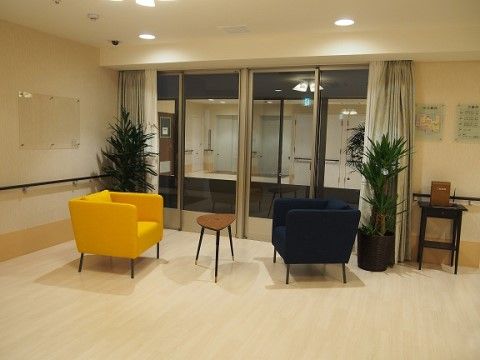 小さなテーブルを挟んで、黄色と黒のモダンな一人掛けソファーが２脚置かれた談話スペースである。窓際には大きな観葉植物も置かれている。