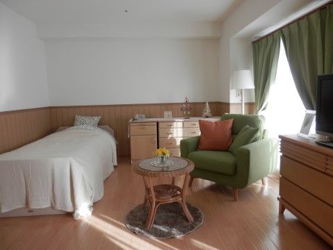 介護用居室は広々としており、左側にはシングルベッド、右側には緑色のソファーと丸テーブルが並べられている。