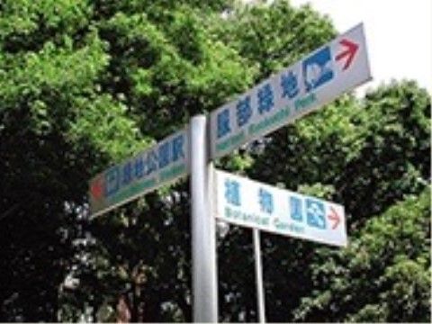 施設の正面には大きな緑地公園があり、敷地内は案内標識が建てられている。白い標識に、青色で文字が書かれている。