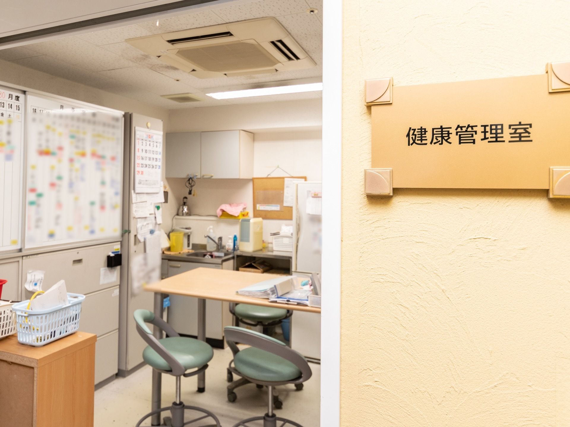 健康管理室にはテーブルを置き、回転式の椅子を置いている。側面がボードの収納庫を備え、壁際に流し台を設置している。