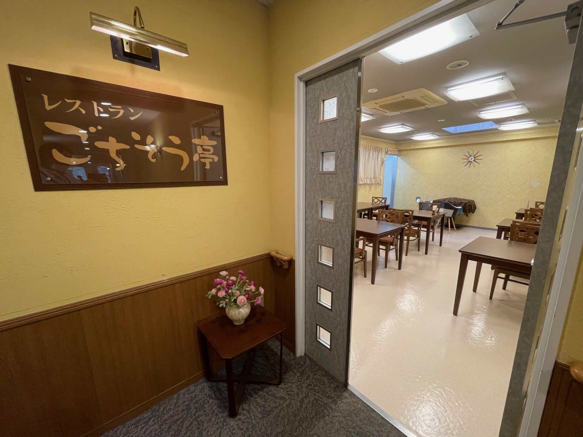 ダークブラウンのテーブルセットを並べている。天井の中央にエアコンを備え、その両側に長方形の照明が並んでいる。