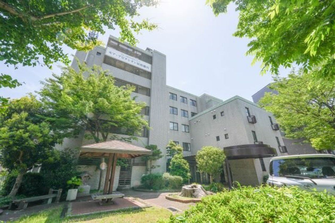 植込み看板を設置し、重厚な屋根の玄関ポーチがある白い色の建物