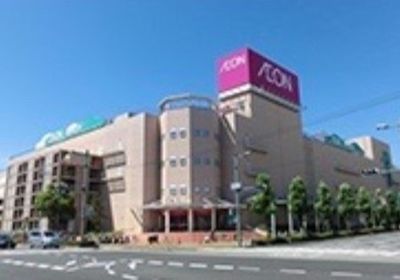 大型のショッピングモールの外観である。４階建ての建物で壁の色はベージュ系である。建物の屋上には看板があり、赤字に白色で店名が表示されている。