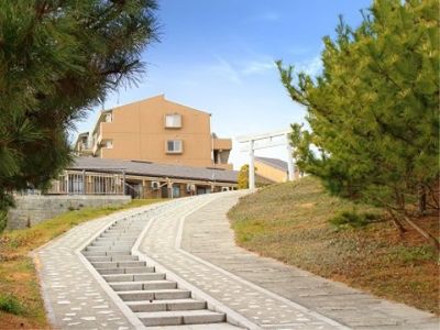 石造りの階段が神社の鳥居につながっており、施設の建物が見えている。階段の周囲には緑の木々があり、自然が豊かな環境である。