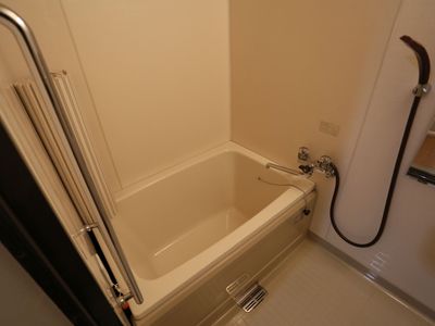 シンプルなデザインのユニットバスである。黒のシャワーを備え、横側に鏡を設けている。お一人がのんびりと入浴を行える広さである。