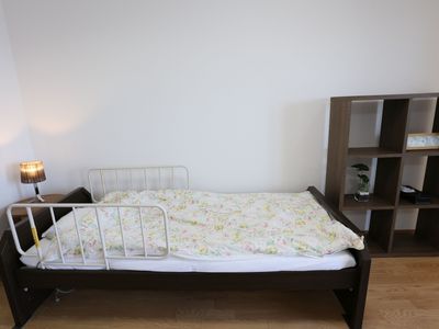居室の壁際にベッドを配置し、横にインテリア家具を備えている。枕元の方に丸テーブルを設け、その上に小さめのスタンドを置いている。