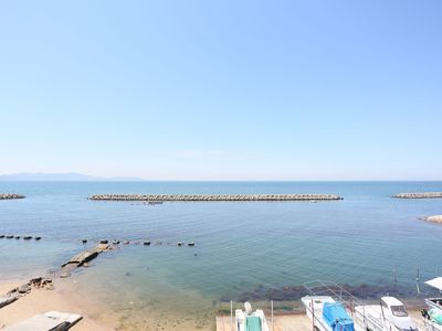 青空と海が一面に広がり、水平線の向こうには島の影が見えている。沖寄りにはテトラポッドが完備され、岸辺には漁船が停泊している。
