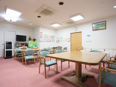 ピンク色のじゅうたんが敷かれた部屋。正方形の机と緑色の座面の椅子が置かれている