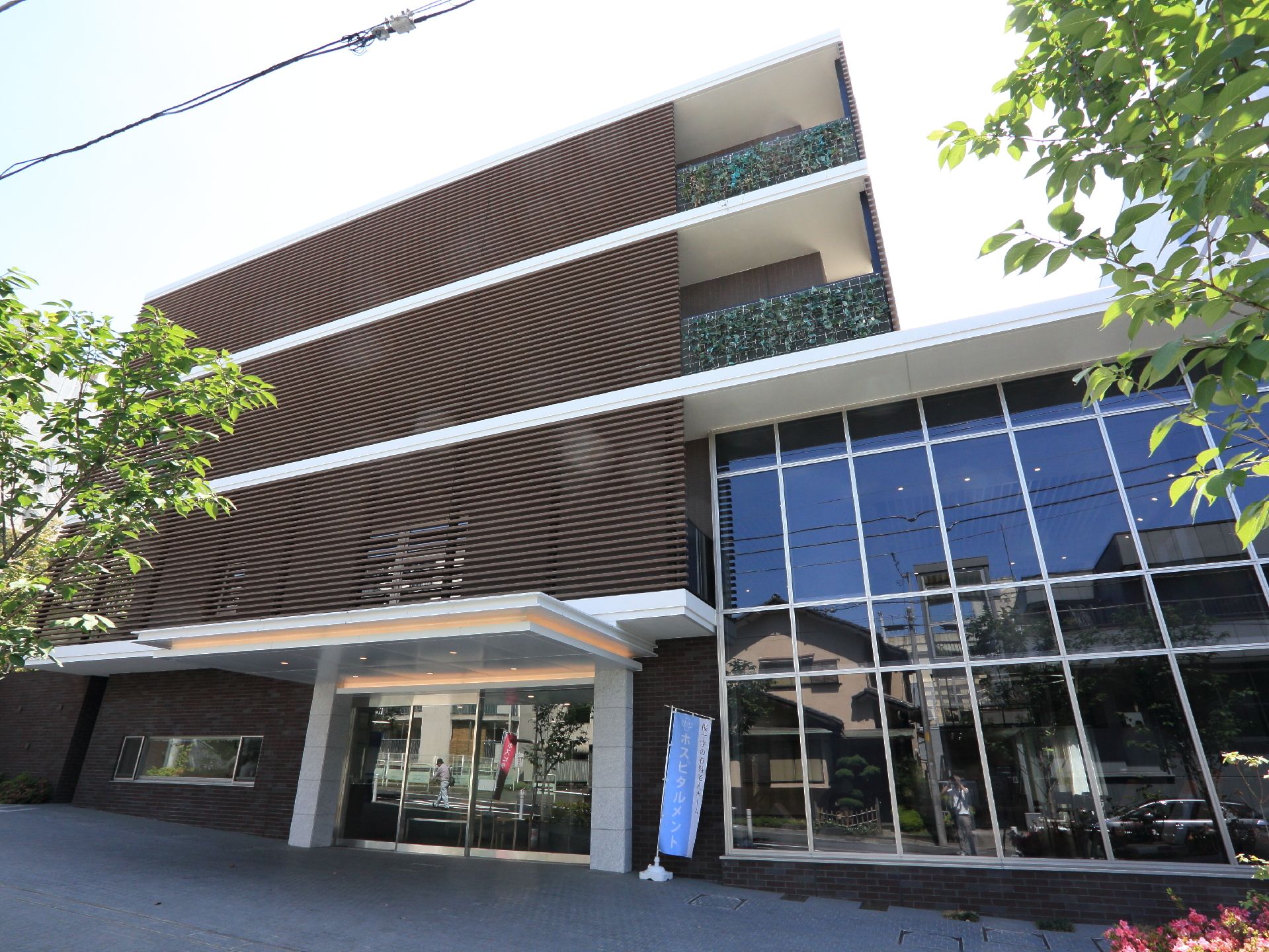 木調の目隠しルーバーやガラス張りの吹き抜けが特徴的な４階建ての建物