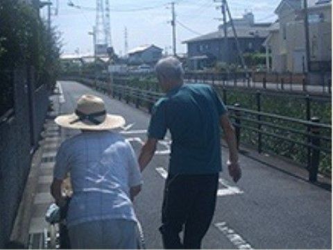 住宅街を通る真っすぐな道路を歩く帽子をかぶった女性と、並んで歩く男性