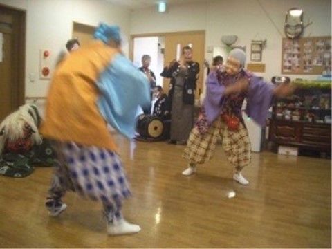 フローリングの屋内で、衣装を着て音楽に合わせて舞踊を披露する人々