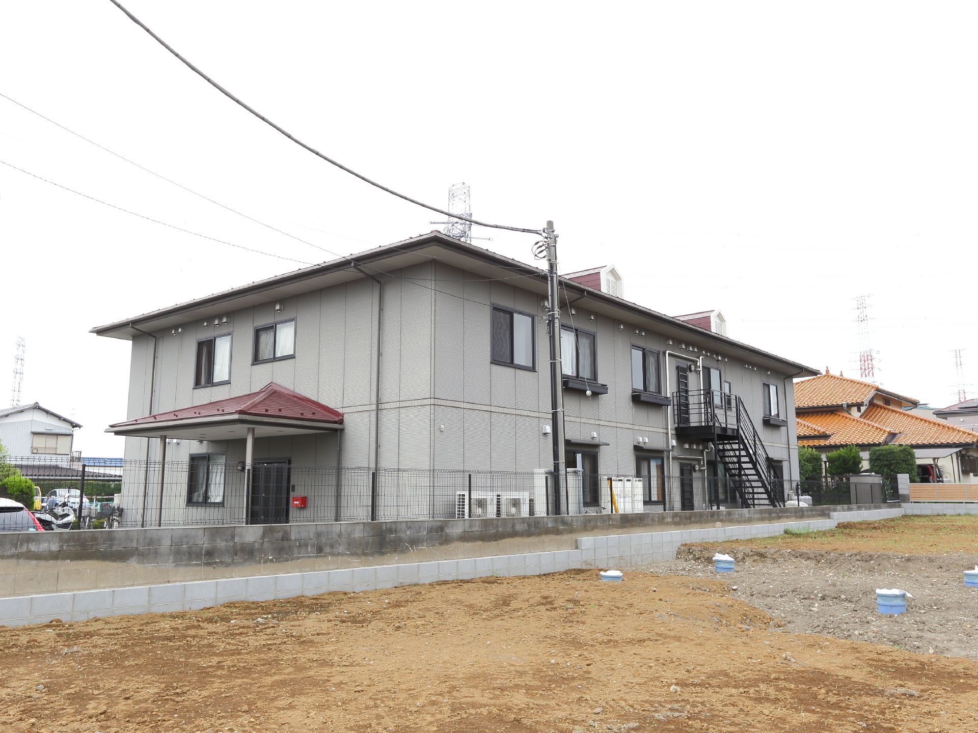 2階建ての建物には外階段もあり、直接２階への出入りが可能になっている。横は空き地になっている。玄関には屋根が付いている。