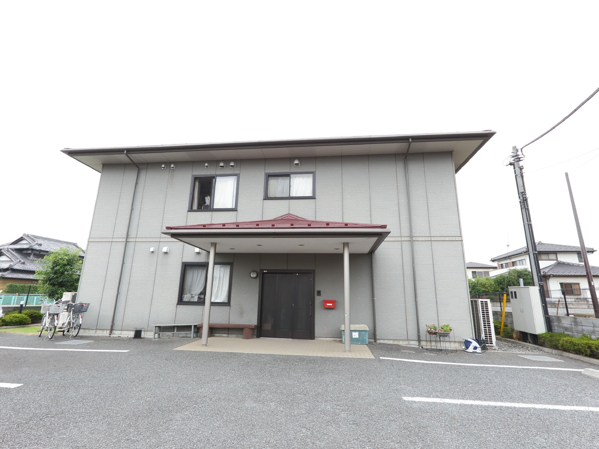 建物はグレーで玄関扉は黒っぽくシックなイメージになっている。扉の横には郵便受けがある。屋根が付いていて雨の日も車への乗降がしやすい。