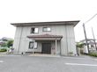 建物はグレーで玄関扉は黒っぽくシックなイメージになっている。扉の横には郵便受けがある。屋根が付いていて雨の日も車への乗降がしやすい。
