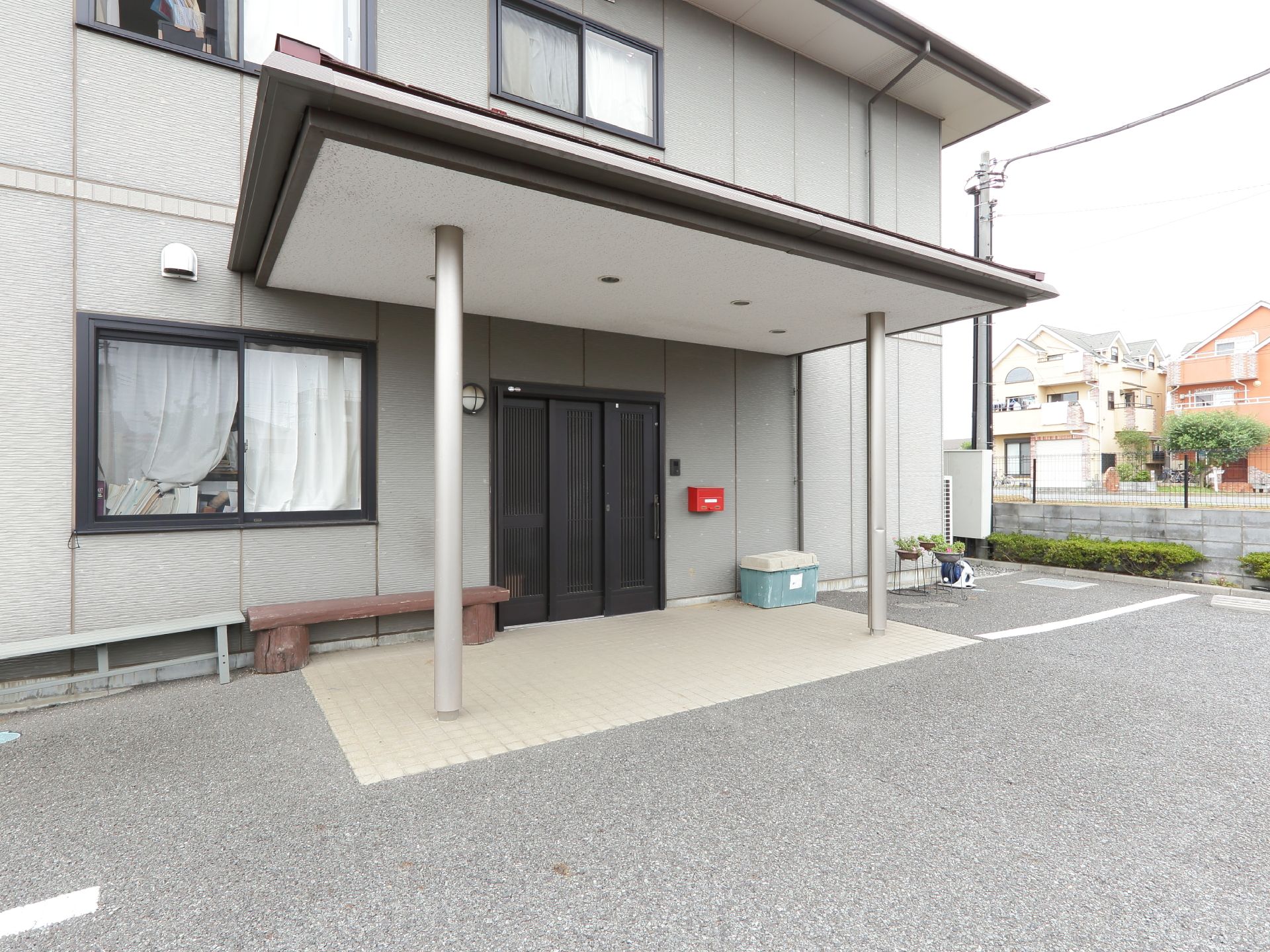 3枚の引き戸になっている玄関の扉。玄関の横には窓がある。玄関前には屋根があり雨の日も安心できる。ベンチが2つある。