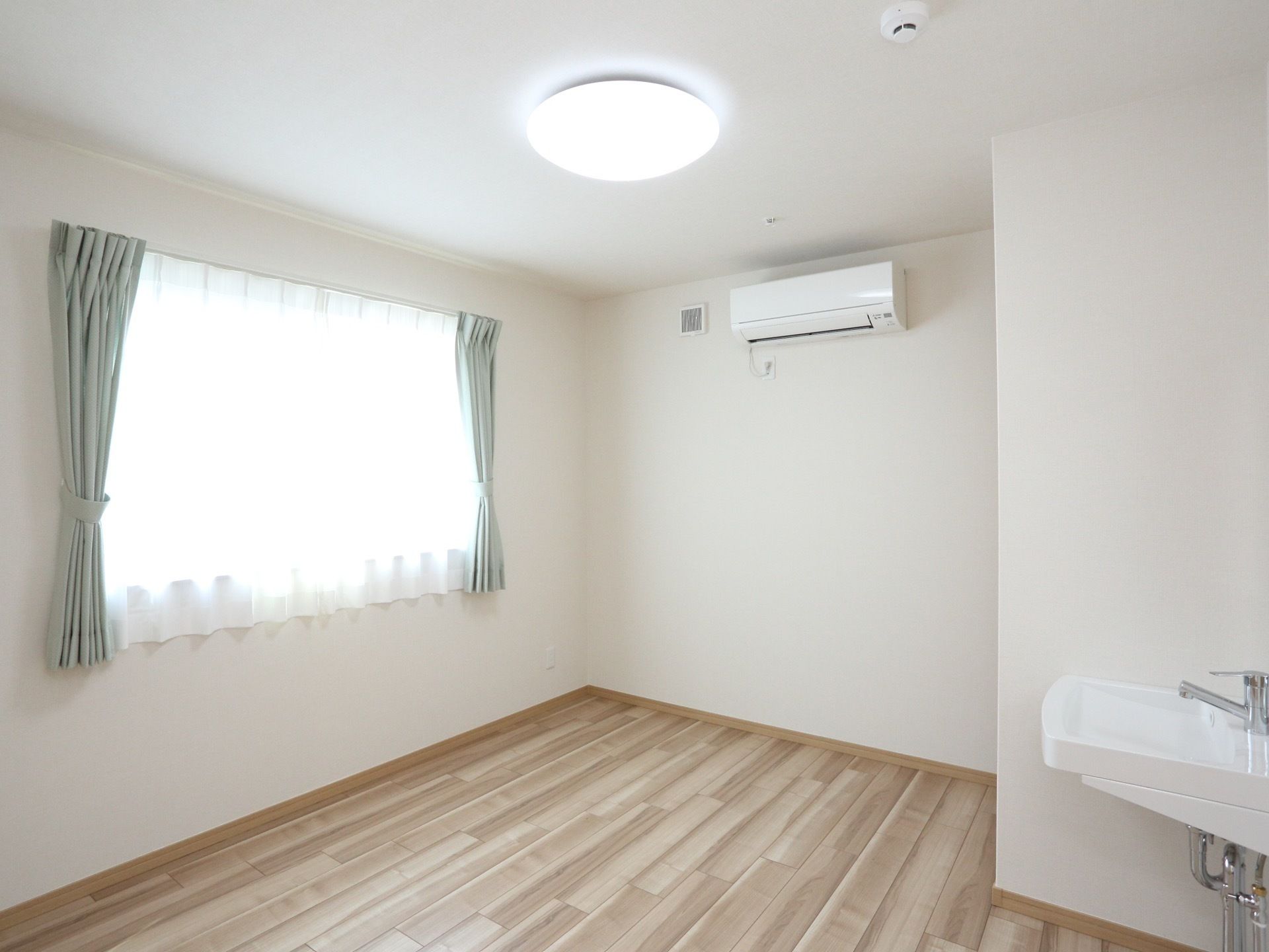 腰高窓がある、明るい色の木肌を活かしたフローリングの部屋
