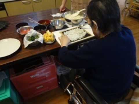 車椅子に座って、テーブル上に材料を広げて料理を行う入居者様