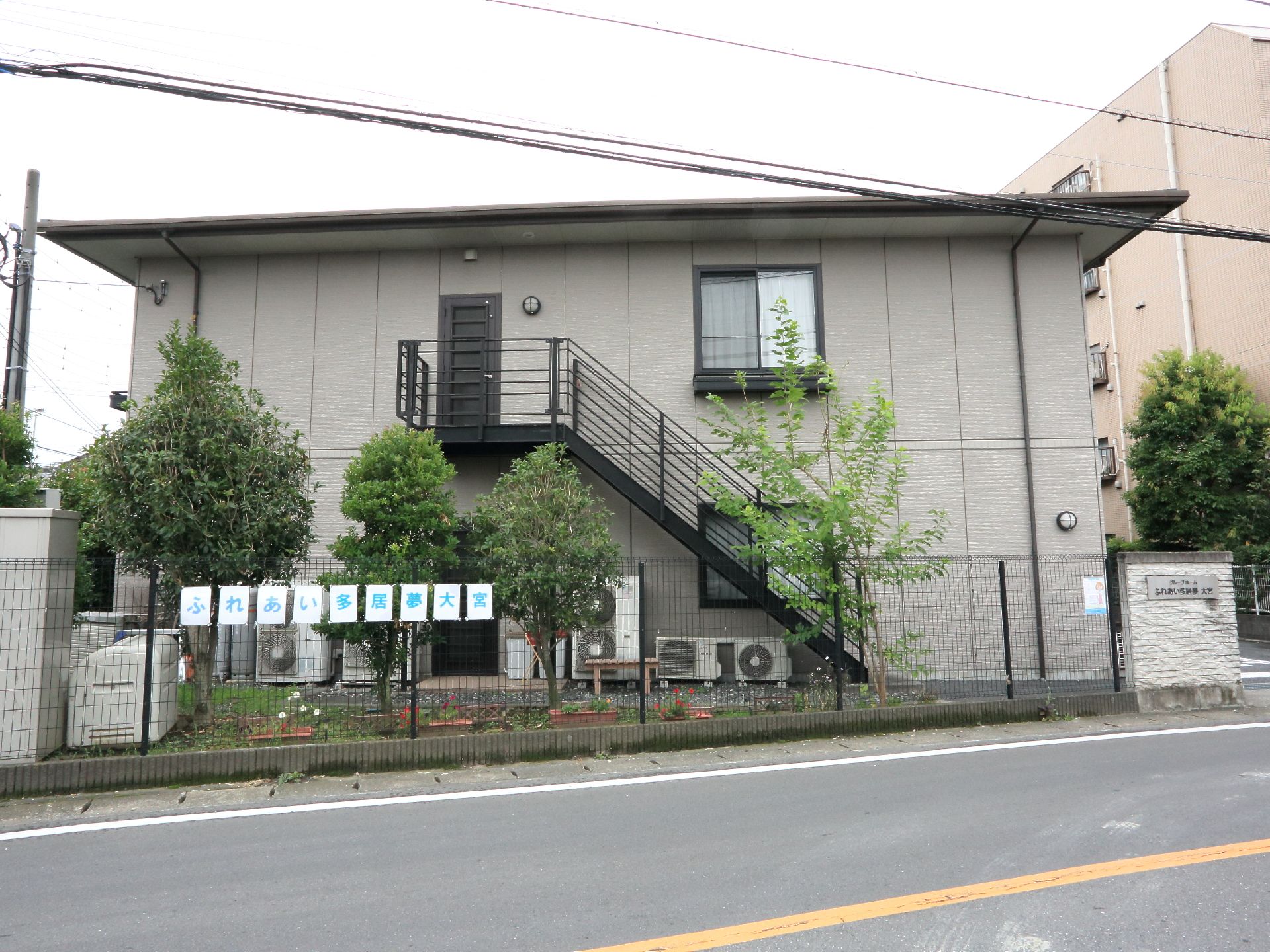 施設を道路に面した側面から見たところ。黒い非常階段と空調の室外機が貼り付くように設置されているのが分かる。