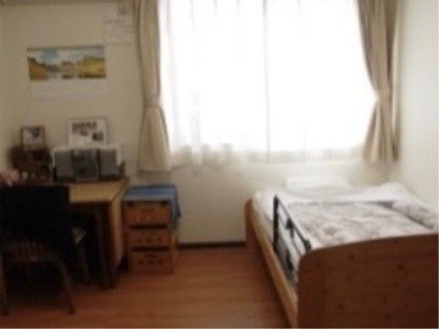 居室には木目が見えるベッドを置いている。窓の横にはデスクを配置して、読み物や書き物ができる場所を作っている。