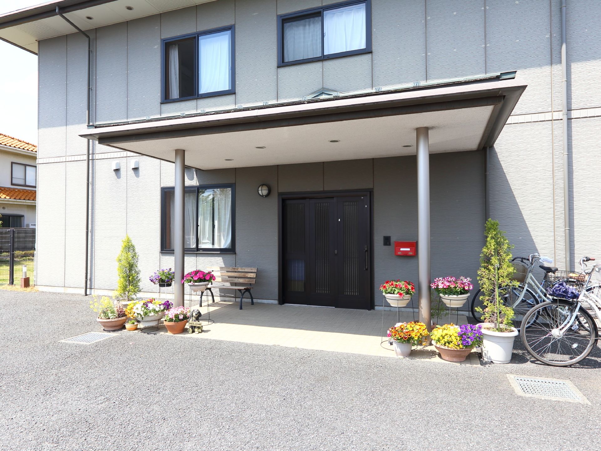段差の無い地面に、色とりどりの花が咲く鉢植えを飾った玄関ポーチ