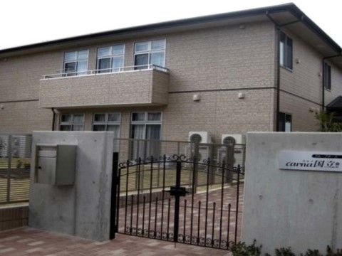 ２階建ての建物で中央付近に窓が並び、ベランダが付いている。外壁の色はベージュで、建物前にはお洒落な門が設置されている。
