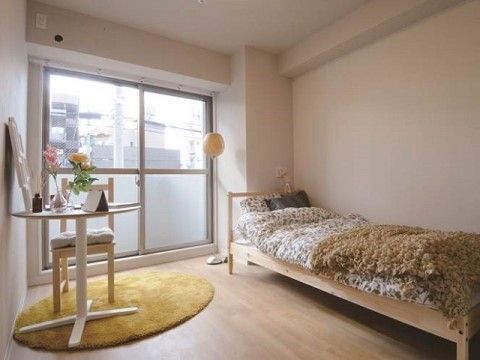 壁際にベッドが置かれている。ベッド横にスタンドライトがあり、丸いラグが敷かれてテーブルセットが用意されている。