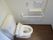 茶系の床で白い壁の清潔なトイレである。リモコン式の温水洗浄便座付きで手すりや緊急通報ボタンも設置されている。