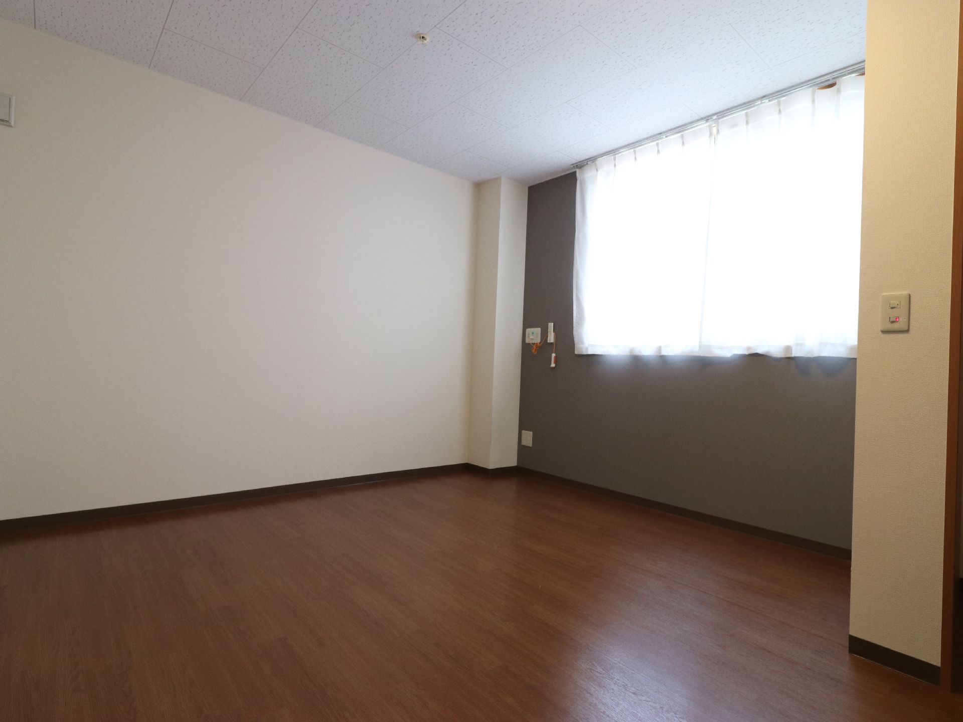 オフホワイトの壁とブラウンの床が、落ち着いた雰囲気となっている部屋である。窓の横には、ナースコールのボタンが付いている。