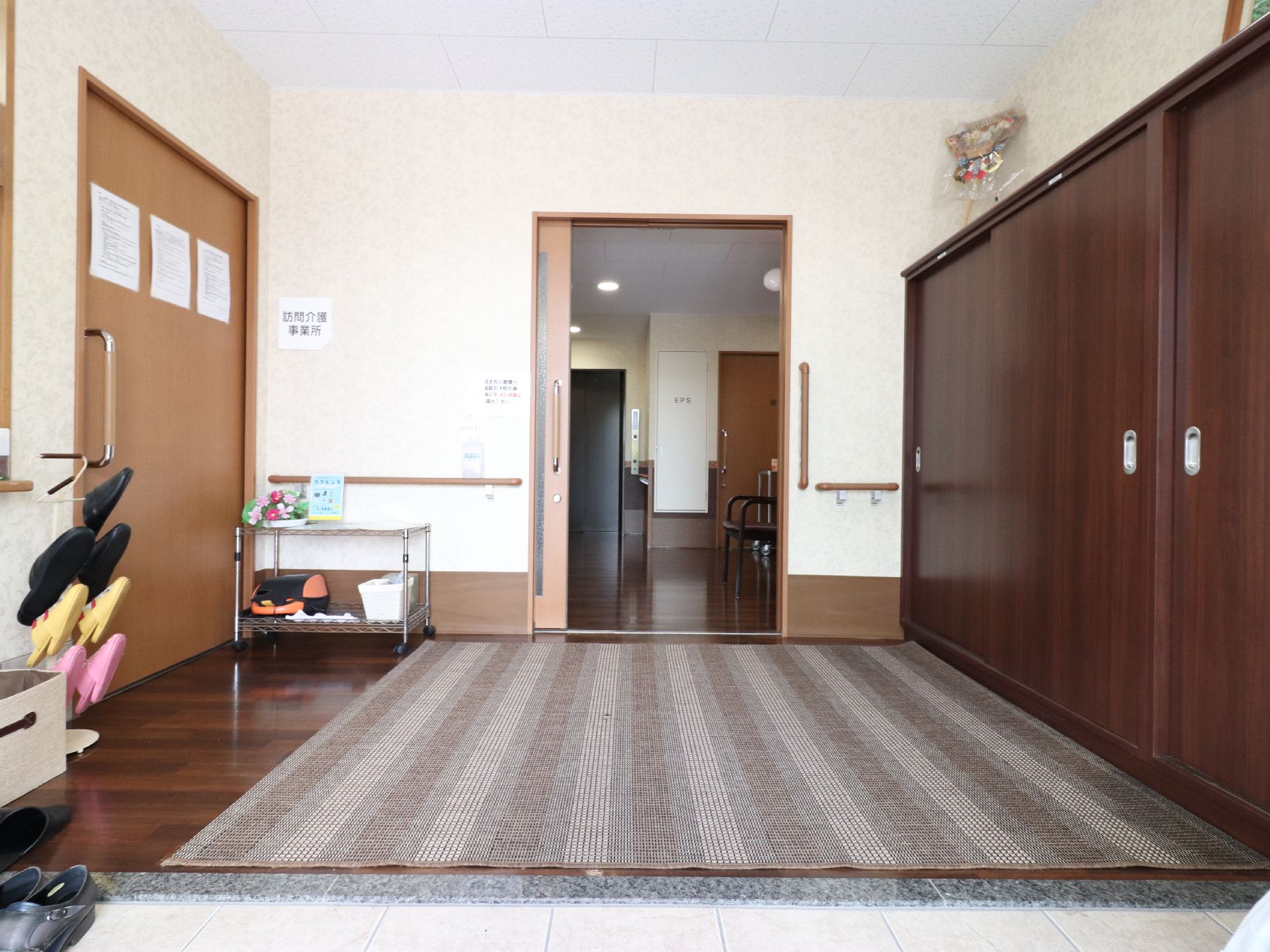 茶色のシューズボックスの前には、ベージュ色のカーペットが敷いてある。スリッパ立てには、ピンクや黄色の子供用の物もある。
