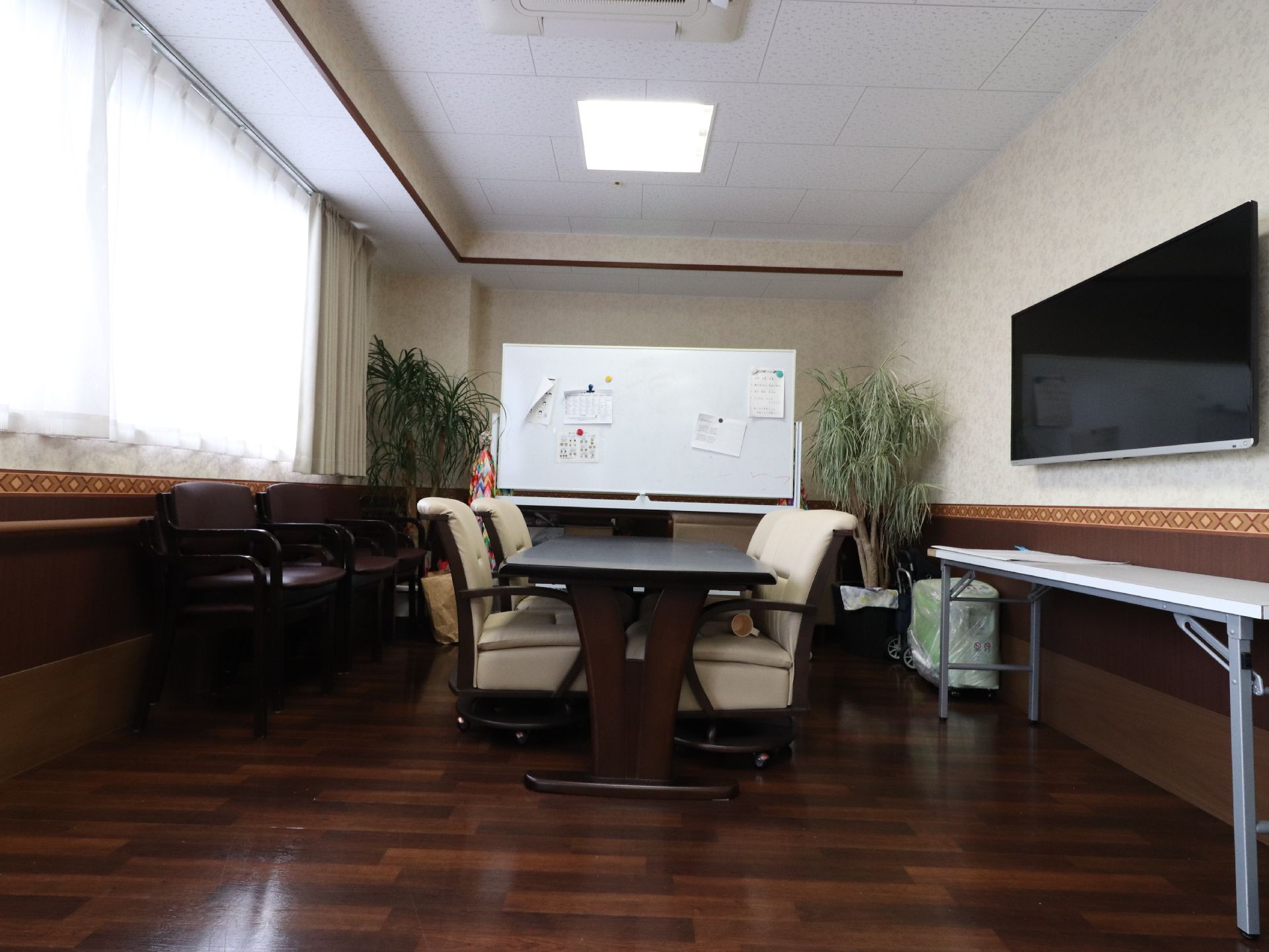 木目調デザインの床が落ち着いた雰囲気の談話コーナーである。ホワイトボードには数枚の書類が貼ってあり、横には観葉植物もある。