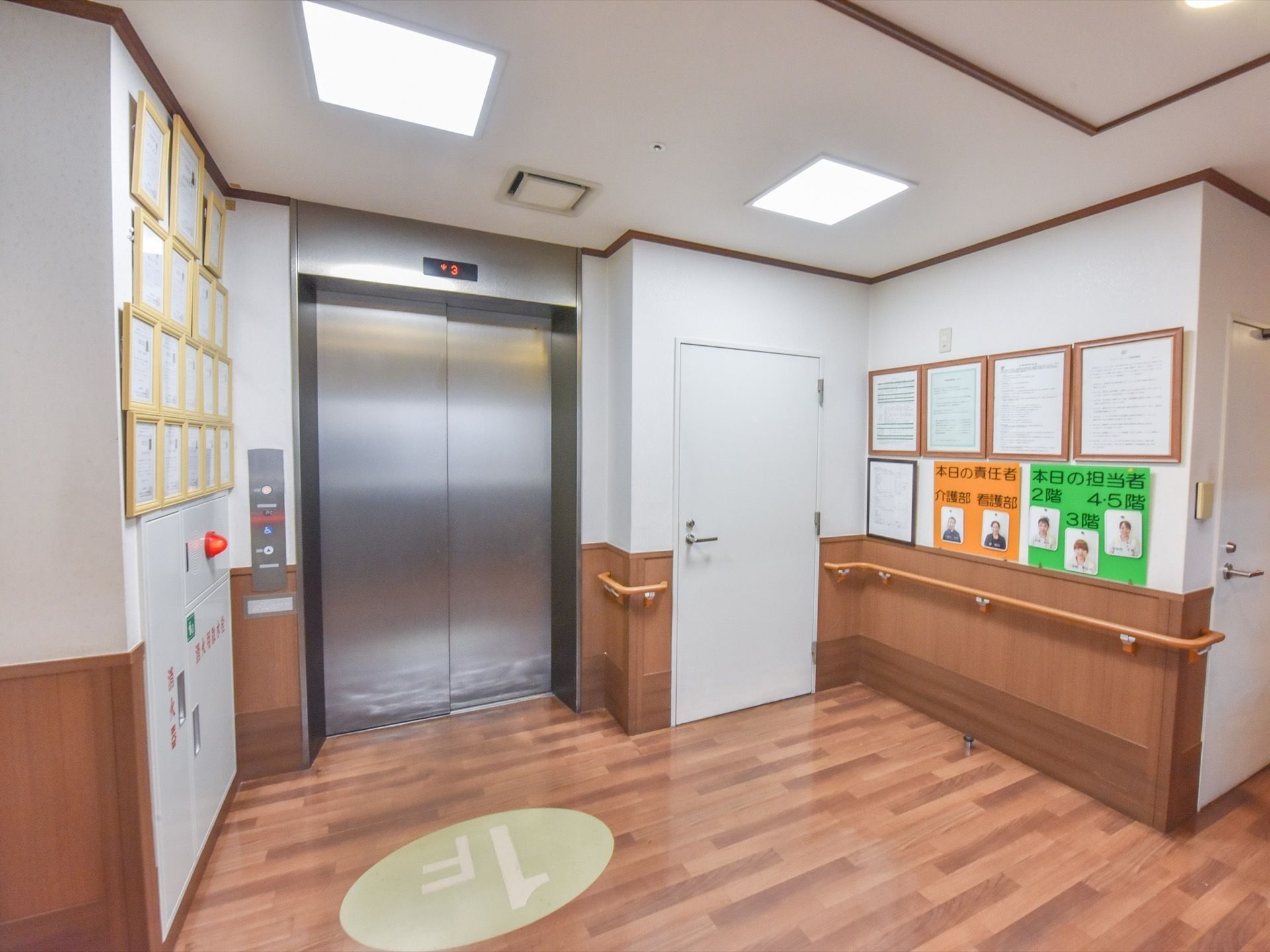エレベーターの床には、1Fという階数が表示されている。右側にはスタッフの責任者や担当者の紙が貼られている。